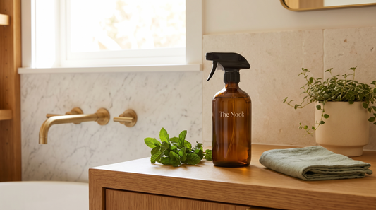 Refillable amber-glass The Nook mint natural cleaner with fresh mint sprigs and a sage-green cloth on a honey-oak counter