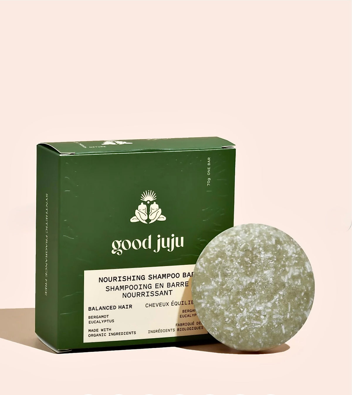 A green rectangular box of Good Juju Nourishing Shampoo Bar next to a round, textured green shampoo bar on a solid pale pink background.